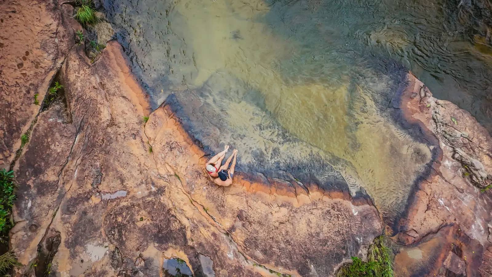 Vista aérea de um casal sentado nas pedras à beira do rio de águas cristalinas da Pousada Rancho da Princesa